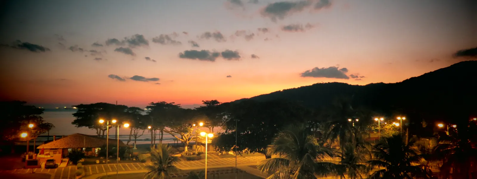 Vista aérea da praia e do bairro de Guaiúba, no Guarujá, com mar azul e vegetação ao redor